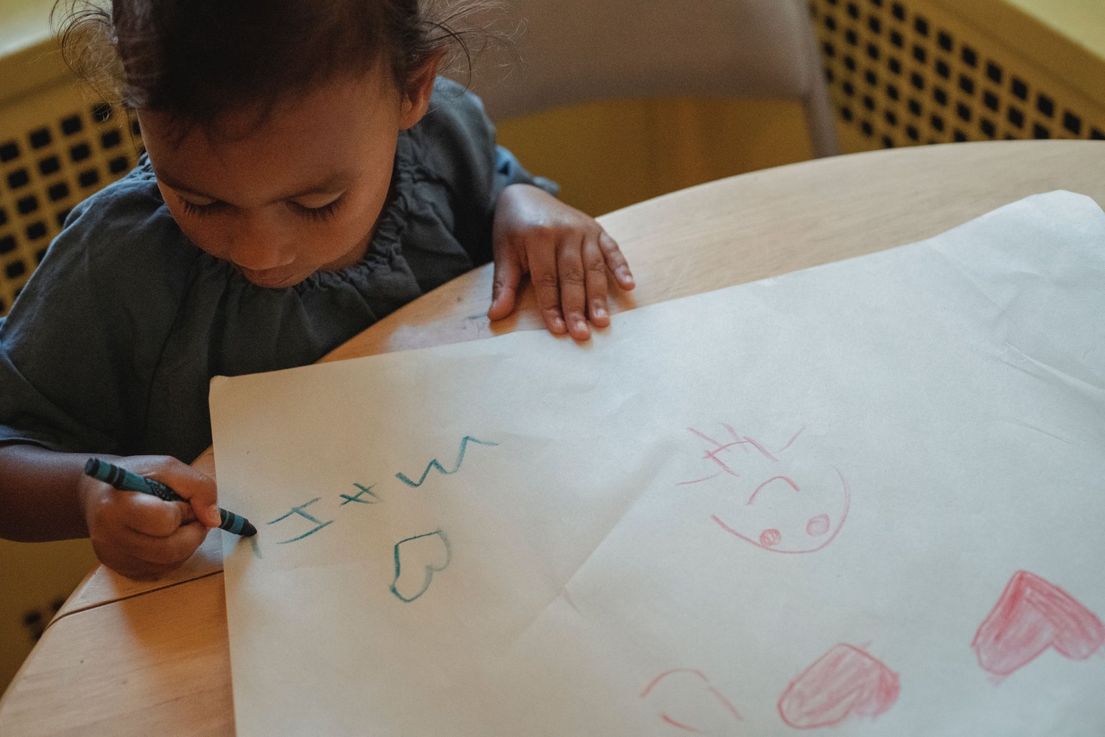 A child drawing with crayons on white paper at a table