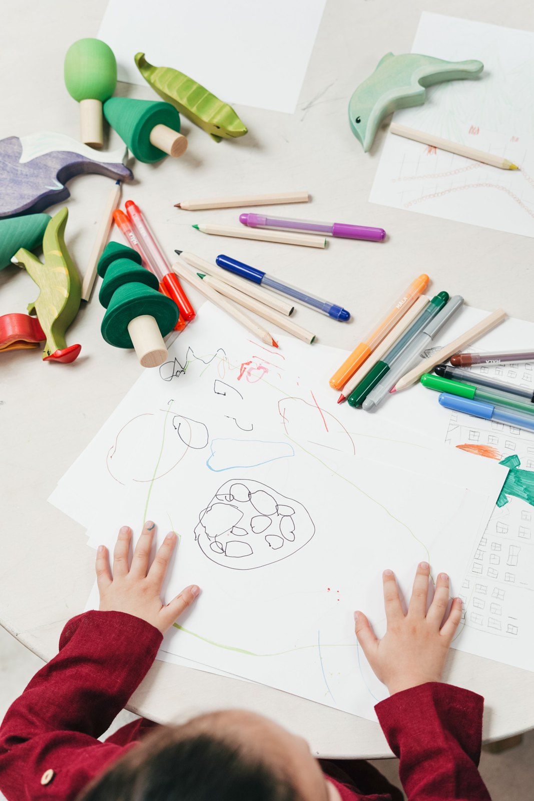 A child using colored pencils on paper beside wooden toys
