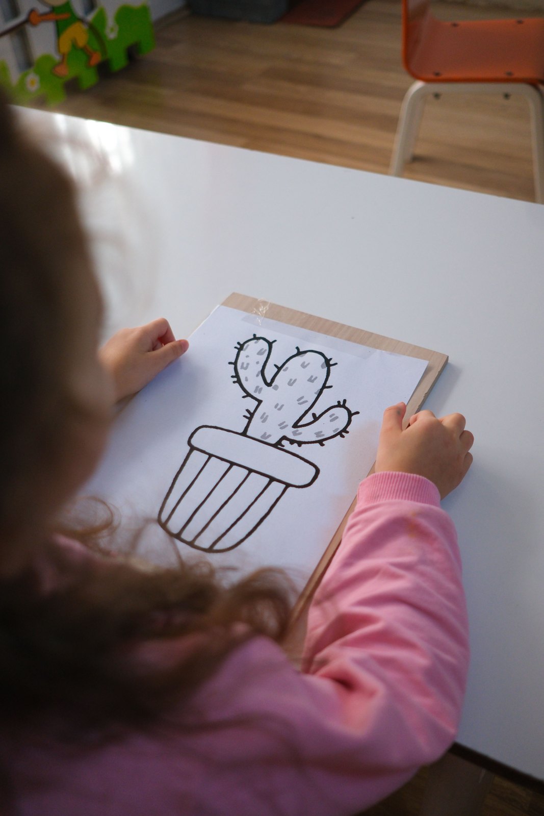 A child coloring an outlined cactus on white paper