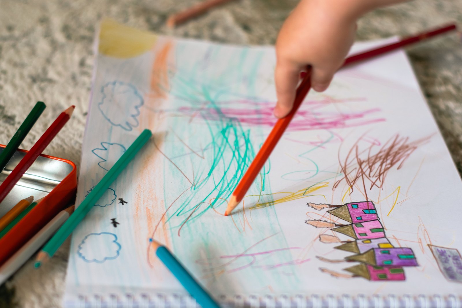 Children’s hands adding colored pencil marks to drawings on paper
