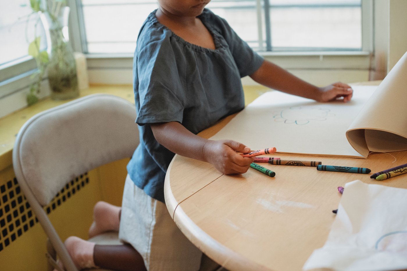 A child drawing with wax crayons on paper at a wooden table.