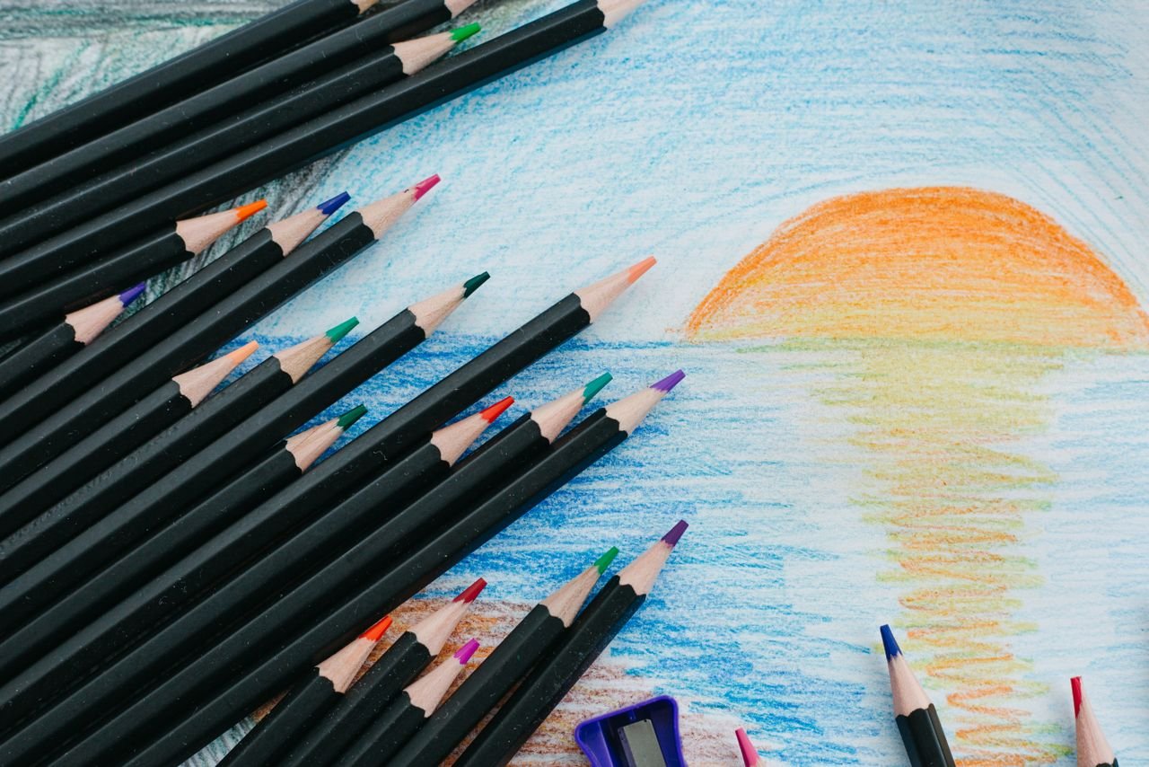 Colored pencils resting on a drawing of a sunset over water.
