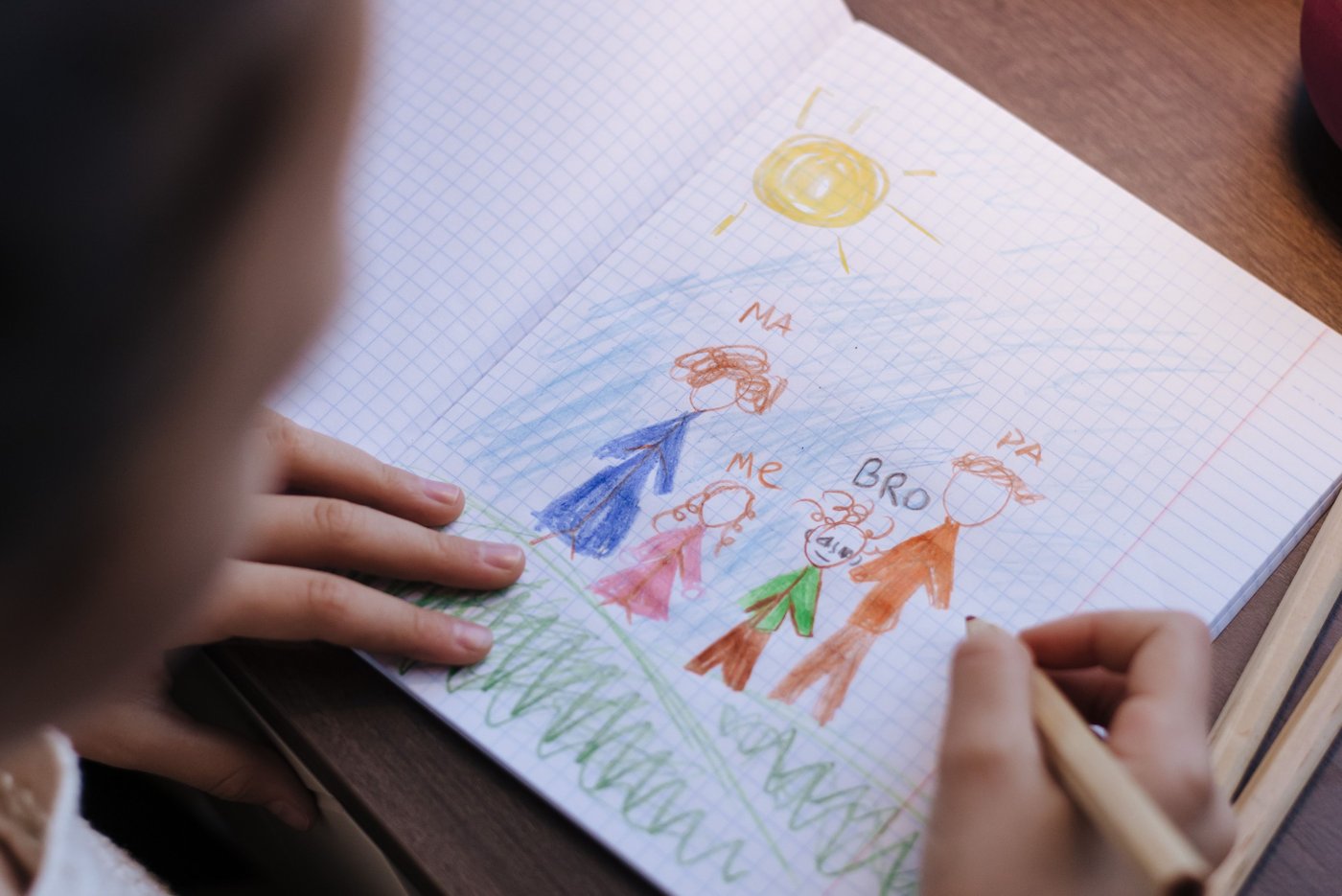 A child drawing a family portrait with crayons in a notebook.