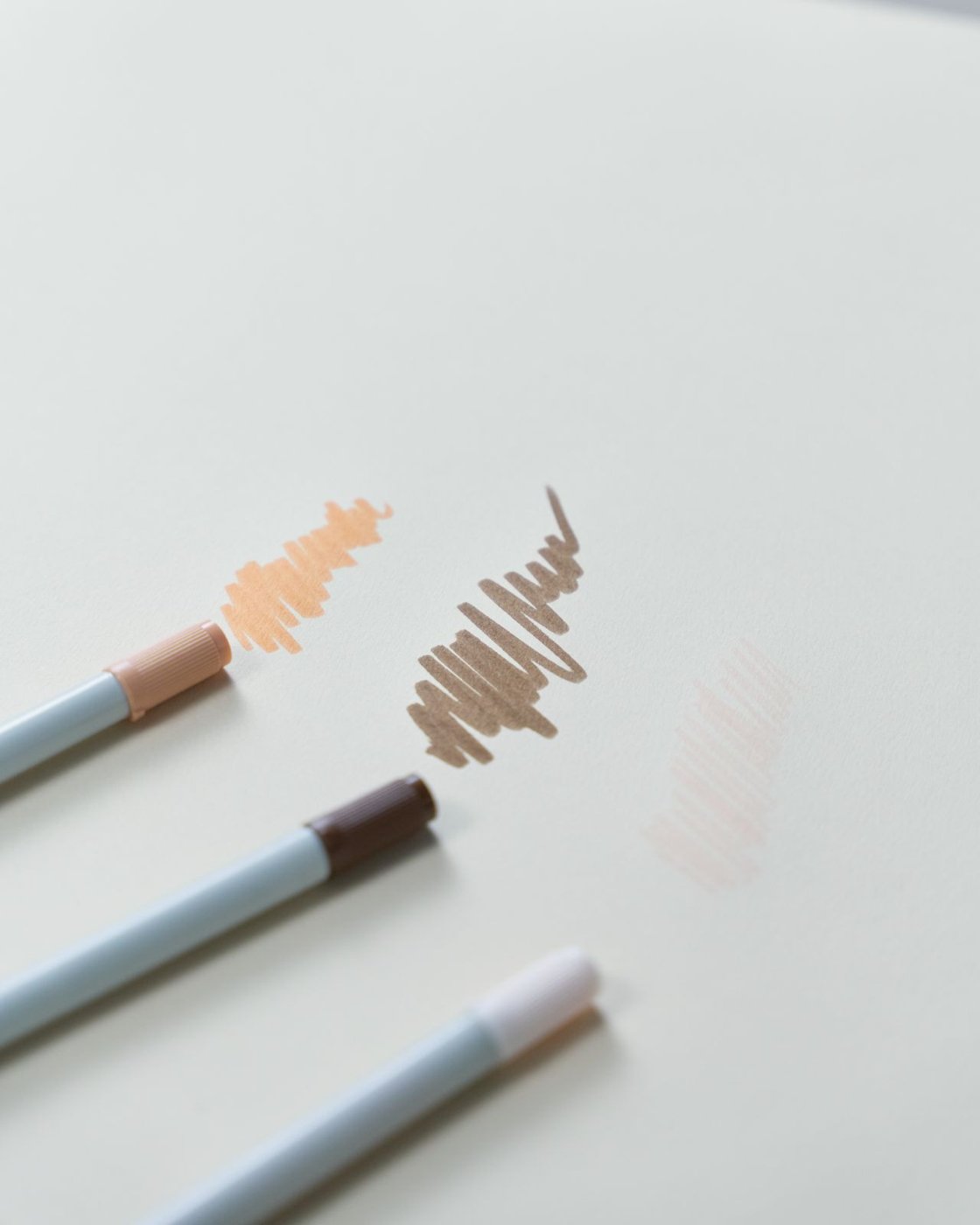 Three colored pencils beside scribbles on a white surface.