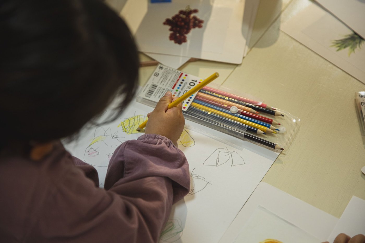A child coloring on white paper with pencils spread nearby