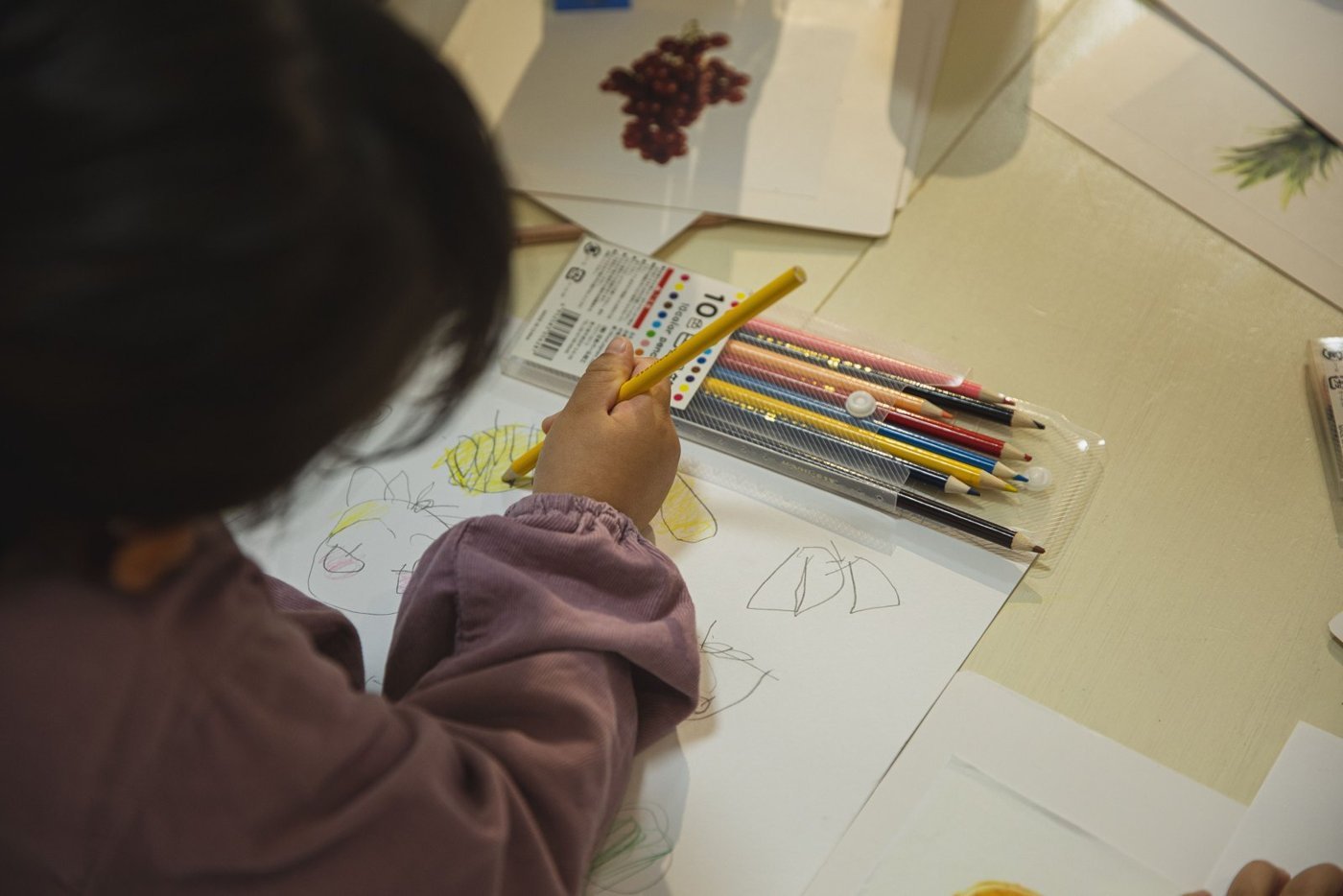A child coloring on white paper with pencils spread nearby