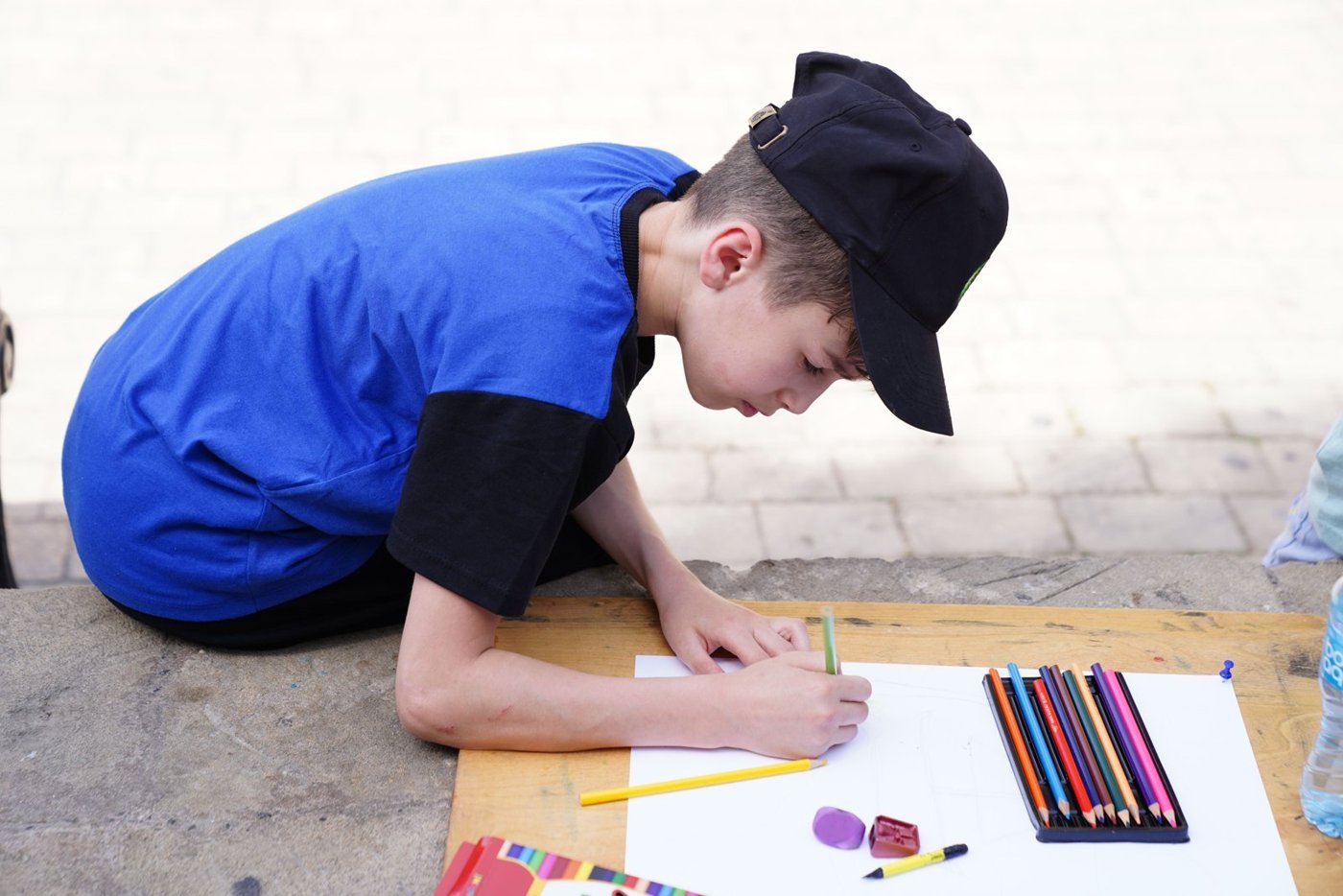 A child in a blue shirt drawing on paper outdoors